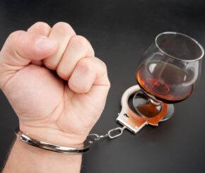 A hand locked to glass of alcohol by handcuffs